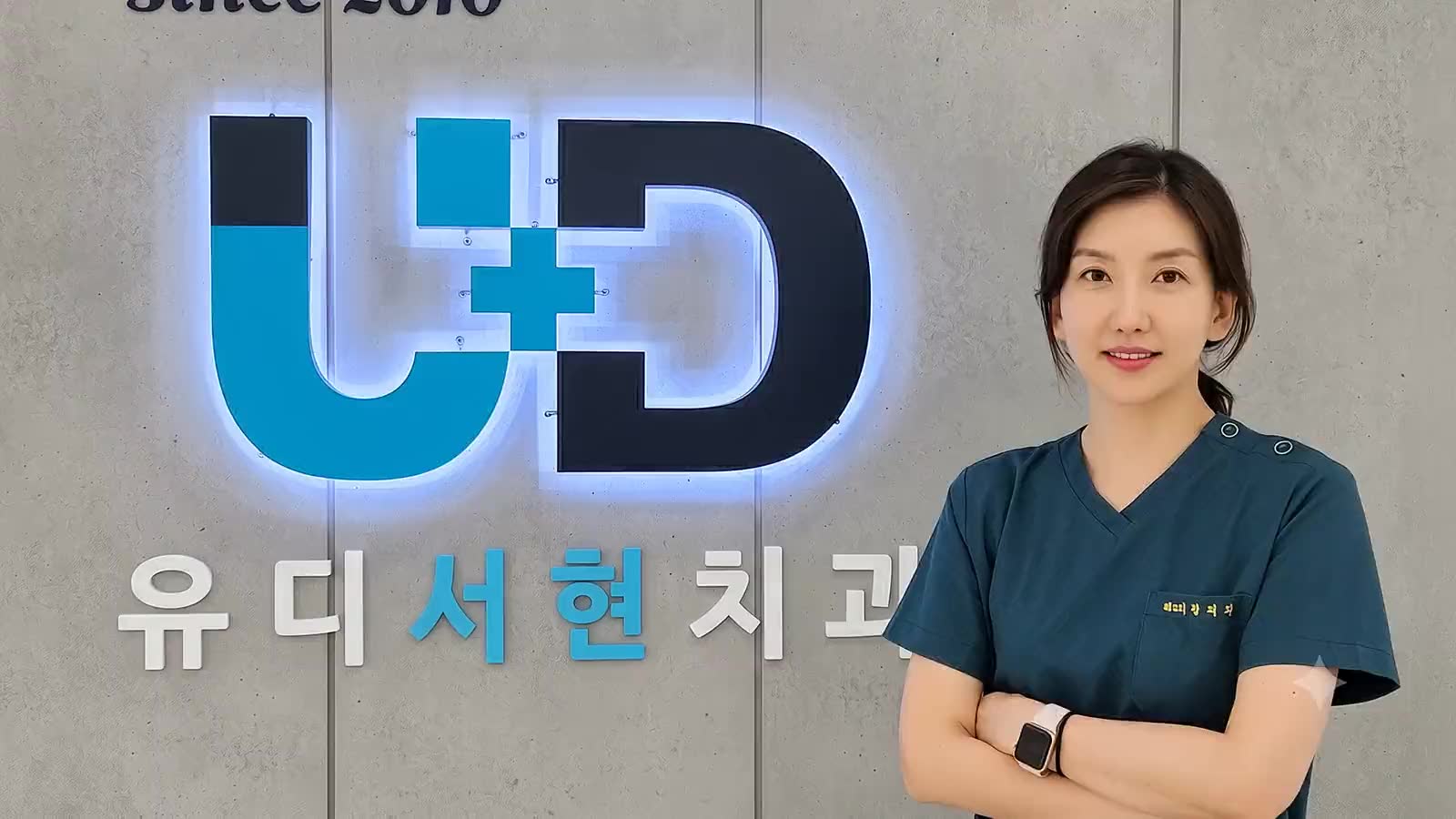 유디서현치과 실내 U+D 사인(since 2010) 앞에 선 황혜진 대표원장 — 분당 서현현대프라자 3층